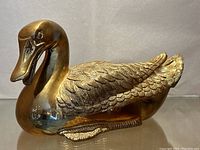 Front and side view of the vintage cast brass duck sculpture, showing polished brass surface and detailed feather engraving.