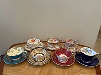 Full view of seven assorted teacup and saucer sets displayed on wood surface