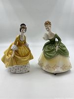 Pair of Royal Doulton figurines Soiree (yellow dress) and Coralie (green dress) shown side by side.
