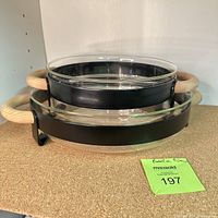 Two nested Boda Nova serving dishes with glass inserts and wooden handles on black metal frames.