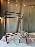 Full view of wooden blanket rack and embroidered footstool beside it on patterned carpet.