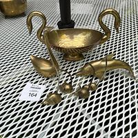 Photo of the entire brass lot showing the double swan bowl, dolphin, and four mice figurines on a white metal table.