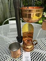 All three copper items displayed on a metal table outdoors: hanging planter, chamber candlestick, and copper mug
