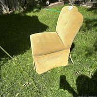 Side angle showing the gold velvet slipper chair's scalloped back and skirted base sitting on grass.