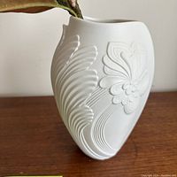 Side view of white ceramic vase showing embossed floral pattern and abstract wave lines.
