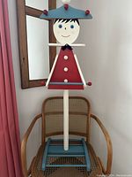 Full view of vintage wooden child's valet clothes hanger featuring novelty character design, sitting on chair with wicker back