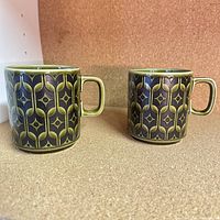 Photo of two vintage Hornsea mugs with green and black geometric design placed side by side to show whole set