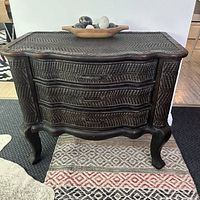Front view of rattan chest of drawers showing three curved drawers with metal handles and carved legs.
