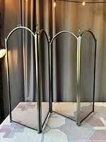 Front view of the four-fold brass framed fireplace screen with black fine wire mesh panels placed on a surface with curtain backdrop.