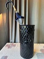 Full view of vintage black ceramic umbrella stand holding a closed Knirps umbrella with curved handle