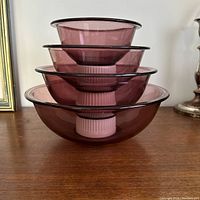 Side view of four nested cranberry glass bowls showing size gradation and black rim detail.