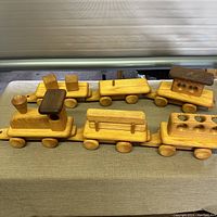 Top view of handcrafted wooden train set showing all train cars lined up in a row on a greenish fabric surface. Cars have removable wooden blocks and logs.