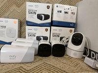 Unboxed bullet and dome cameras in front of three protective skin boxes and one battery life hub box