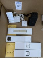 White dual wireless charging stand and black vertical stand at top; Series 7 watch box open center; unopened gold band box; empty watch box below