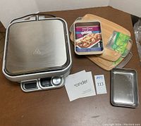 Photo of Cinder Precision Grill, two wrapped Farberware bamboo cutting boards, and two small casserole dishes, one Nordic Ware and one metal tray.