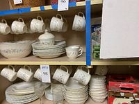 Shelf displaying a variety of Arcopal Victoria dishware including plates, bowls, and cups with floral pattern and ruffled edges, also glassware visible.