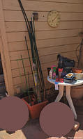 Photo of various gardening supplies including plant stakes, tomato cage, and melamine table with pots and accessories on top.