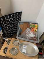 Photo showing three patterned black dish mats, plastic bin containing wood grilling planks, serving platters (wood and stainless steel), and condiment bowls.