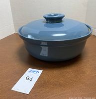 Side view of the dusty blue ceramic covered casserole dish with round knob lid on a brown surface.