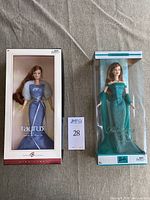Two boxed Barbie dolls side by side: Taurus Barbie in purple sparkly dress with fur stole and Emerald Barbie in green dress.