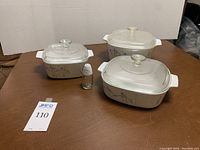 Overview of three graduated Pyrex casserole dishes with lids and matching salt shaker on brown table