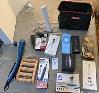Full view of lot showing all items together on the floor including foot sander, wooden foot massager, blackhead remover, ketone monitor, vaporizer, and bag.