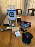 Full view of lot on table showing all items including snow chains box, Tesla cap, mirror, license plate holder, LED kit, shadow light box, and other small boxes/can.