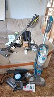Three vacuum cleaners on couch and floor with various parts and accessories laid out