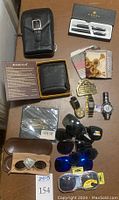 Full overview of lot items including wallets, pens, watches, sunglasses and belt buckle