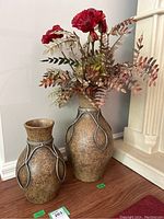 Pair of ceramic vases on hardwood floor near wall, one vase holding artificial flowers.