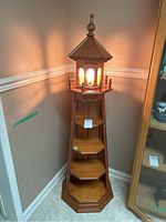 Full view of the wooden lighthouse display shelf illuminated in a corner showing the top light casting a glow, hexagonal shelves and decorative finial on roof.