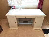 Front view of white double pedestal desk showing single center drawer and cupboard doors on each side.