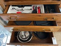 Drawers with various bakeware including cookie sheets, frying pans, a pizza pan, and strainers