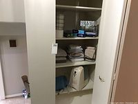 Bathroom closet with towels on shelves and a white Honeywell humidifier on lower shelf