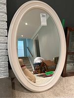 Front view of the off-white oval mirror showing frame and mirror surface reflecting stairs and wall.