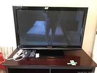 Front view of Panasonic 42-inch flat screen TV sitting on wooden table with remote and power bar alongside.