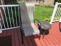 Patio set on wooden deck showing chair with high fabric backrest and small round metal table to the right.