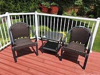 Photo of two dark brown wicker-look chairs and square glass-top side table on outdoor deck.