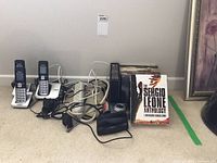 Photo showing two V-Tech cordless phones on base stations, white surge power bar, Canon PowerShot A40 camera, black Westclox electric clock, and a stack of DVD sets including Sergio Leone Anthology.
