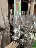 Photo showing 4 tall crystal flutes and 8 wine glasses with intricate pinwheel cut pattern on glass, placed on reflective surface.