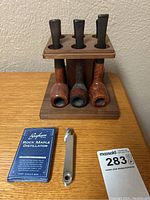 Photo showing three pipes fitted into the wooden stand and cleaning tool with Brigham Rock Maple Distillator pack on the table.