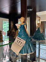 Full view of the Royal Doulton figurine in blue gown holding a fan, displayed in a glass cabinet.