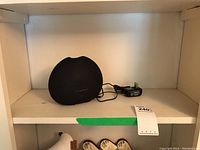 Black SAJE Wellness Aroma Breeze essential oil diffuser with power adapter on white shelf.