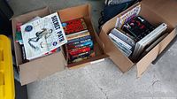 Three cardboard boxes filled with various hardcover and paperback books including a boxed set and assorted titles.