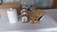 Group view of all items described in the lot: tall white ceramic canister, four birdhouse canisters, glass canister, wooden cheese utensils set, and two owl cups.
