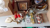Overview of lot items on table showing dresser set, trinket box, perfume bottle, wall clock, fans and handkerchiefs