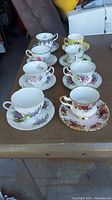Photo of all eight teacups and saucers arranged on a table showing variety of floral designs and styles.