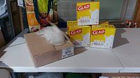 Five boxes of Glad small white garbage bags and one box of clear garbage bags on a white table.