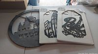 All three metal art items visible on a table, two silhouettes still boxed, circular weathered welcome sign with hanging chain.