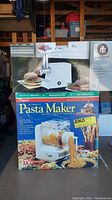 Photo showing the boxed Popeil automatic pasta maker with images illustrating pasta extrusion and drying rack.